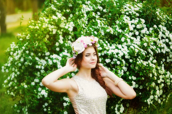 Chica en una corona de flores cerca de un arbusto en primavera — Foto de Stock