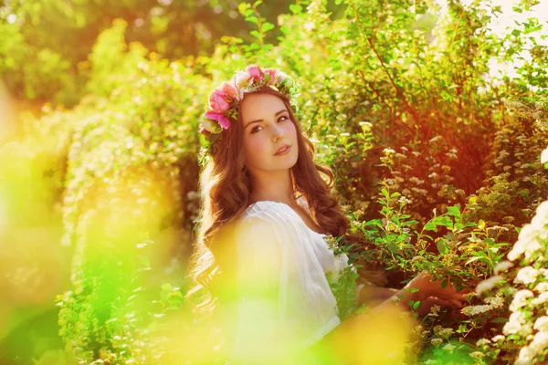Tânără fată frumoasă cu păr lung în coroană florală în grădina de primăvară — Fotografie, imagine de stoc
