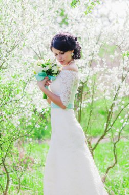 Bahar Çiçek bahçesinde genç güzel gelin. Bir düğün buket bahar bahçe Beyaz giysili bir gelinle