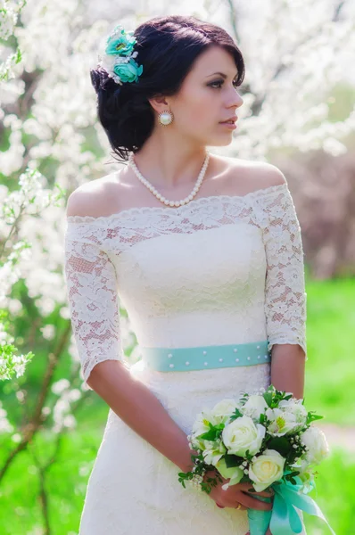 Giovane bella sposa in un giardino fiorito in primavera. La sposa in un abito bianco con un bouquet da sposa nel giardino primaverile — Foto Stock