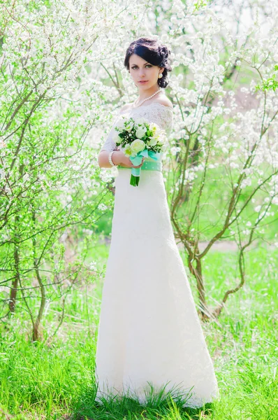 Giovane bella sposa in un giardino fiorito in primavera. La sposa in un abito bianco con un bouquet da sposa nel giardino primaverile — Foto Stock