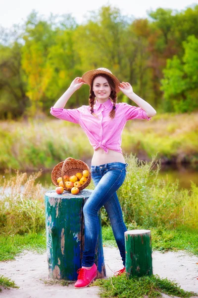 Девушка в соломенной шляпе и яблоках осенью у реки — стоковое фото