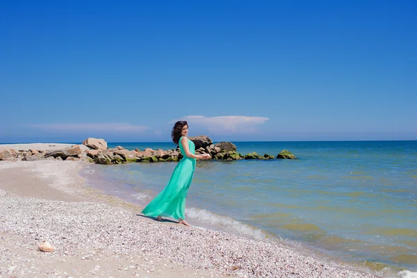 夏のビーチで長いドレスを着た美しい少女。砂の上の青い海の中の少女 — ストック写真