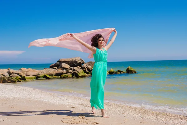 Νεαρό κορίτσι στην παραλία το καλοκαίρι σε ένα όμορφο φόρεμα με ένα ιπτάμενο κασκόλ — Φωτογραφία Αρχείου