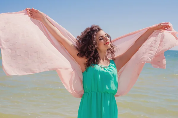 Young girl on the beach in summer in a beautiful dress with a flying scarf