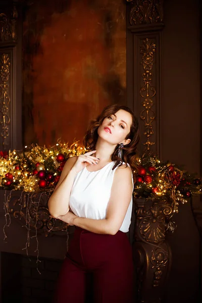 ヘアスタイルと暖炉のそばにクリスマスのために装飾された暗いスタジオで化粧をした夜のドレスで魅力的な若い女性 お祭り気分 クリスマス — ストック写真