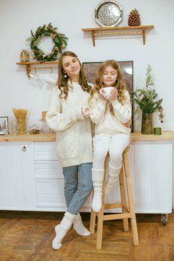 Kızlar mutfakta sıcak kakao dolu süveter örüyorlar.