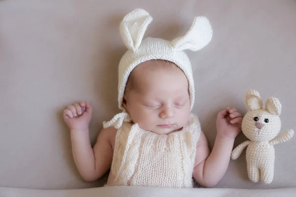 Baby in a knitted rabbit hat with ears and a bunny toy in a beige light blanket. Spring photo. Easter and children. Happy motherhood. Happy easter