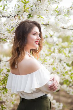 Baharda, güneşli bir havada, kiraz bahçesinde, beyaz, romantik, ipek bir bluz içinde güzel bir genç kız. Bahar ve Moda
