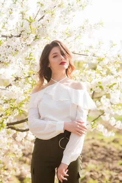 在阳光灿烂的樱花花园里 一个穿着白色浪漫丝绸衬衫的可爱的小女孩 春天与时尚 — 图库照片
