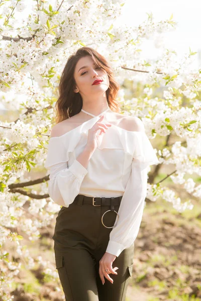在阳光灿烂的樱花花园里 一个穿着白色浪漫丝绸衬衫的可爱的小女孩 春天与时尚 — 图库照片