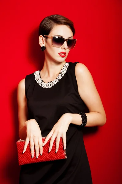 Beautiful girl with a red clutch bag and sunglasses — Stock Photo, Image