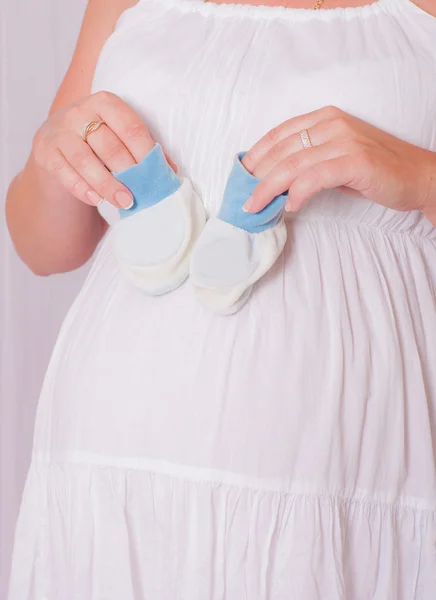 Buik van een jonge zwangere vrouw met blue baby slofjes — Stockfoto