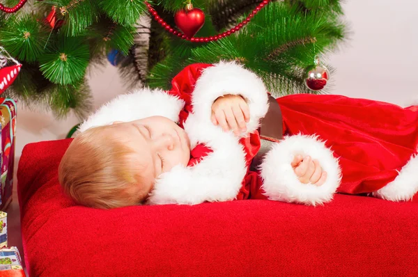 Малыш в костюме Санты спит у елки — стоковое фото