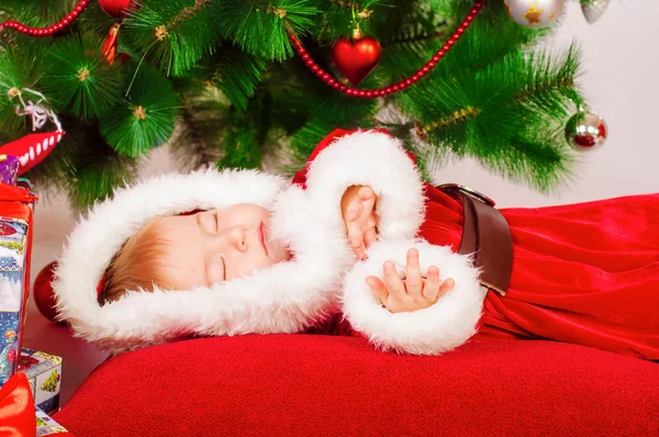 Малыш в костюме Санты спит у елки — стоковое фото