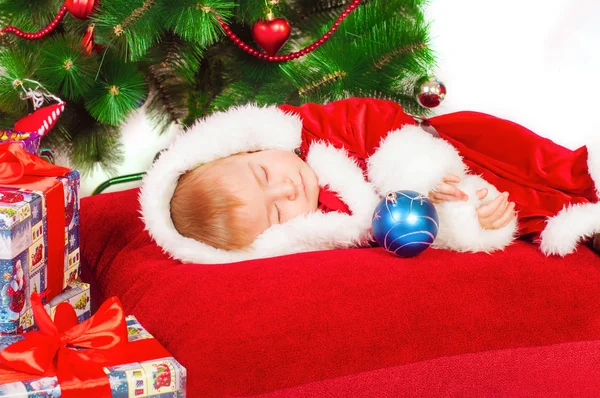 Baby im Weihnachtsmannkostüm schläft am Weihnachtsbaum — Stockfoto