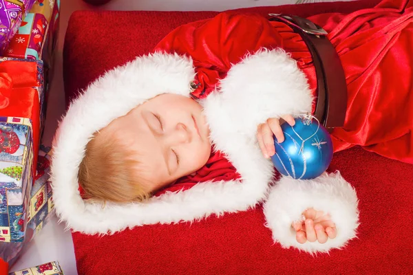 Baby im Weihnachtsmannkostüm schläft am Weihnachtsbaum — Stockfoto