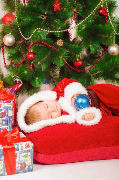 Дитина в костюмі Санти спить на ялинці — стокове фото