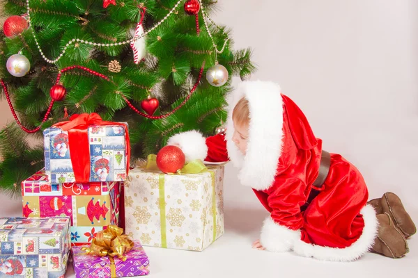 Ребенок в костюме Санты на рождественской елке с подарками — стоковое фото