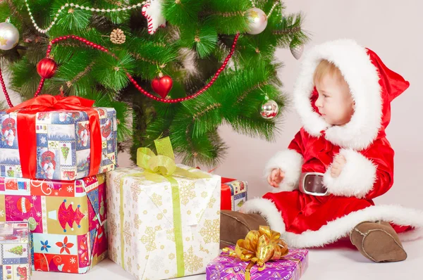 Baby in Santa costume at the Christmas tree with gifts — Stock Photo, Image