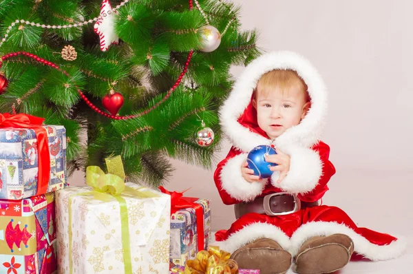 Baby in Santa kostuum op de kerstboom met geschenken — Stockfoto