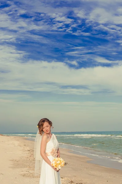 Junge Braut in einem schönen Kleid mit einem Strauß am Strand — Stockfoto