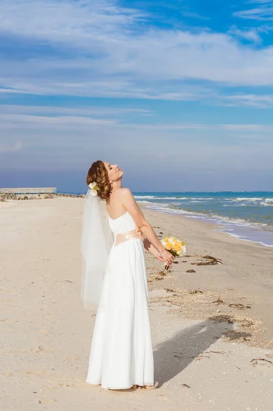 Panna młoda w piękną sukienkę z bukietem na plaży — Zdjęcie stockowe