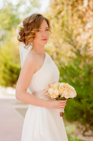 Junge Braut im Garten in einem weißen Kleid — Stockfoto