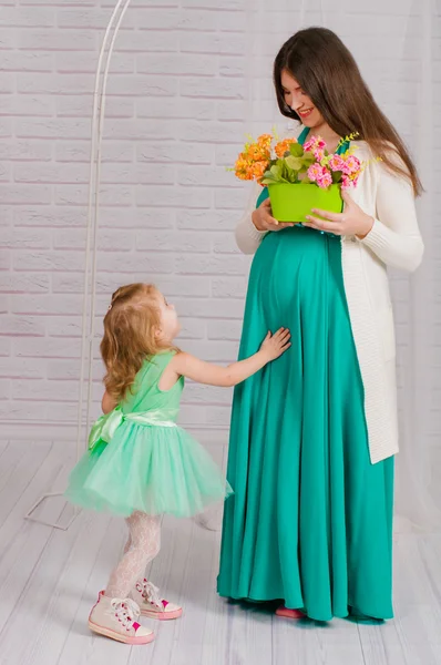 Молодая беременная женщина в бирюзовом платье и маленькая девочка — стоковое фото