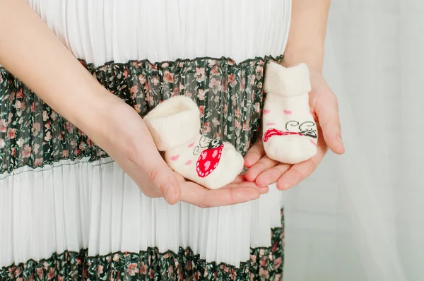 Baby strumpor i händerna på gravid kvinna — Stockfoto