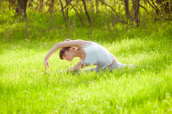 Jeune fille faisant du yoga sur une herbe verte — Photo