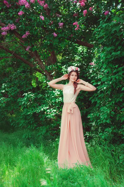 Genç güzel kız uzun elbise ve bir çelenk çiçek leylak Bush — Stok fotoğraf