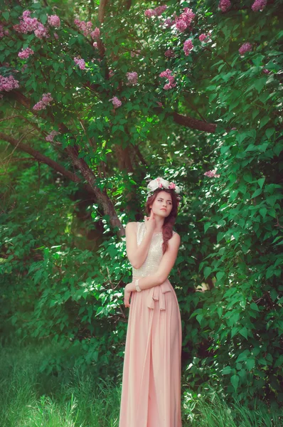 Young beautiful girl in a long dress and a wreath of flowers of lilac bush — Stock Photo, Image