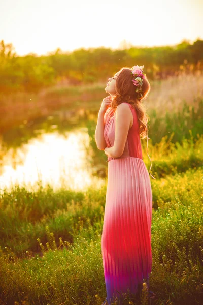 Young girl in flower wreath at sunset by the river in the summer — Stockfoto