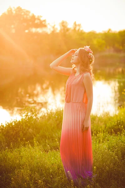 Young girl in a long dress  at sunset by the river in the summer — Stock fotografie