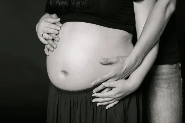 Mains d'hommes et de femmes sur le ventre enceinte — Photo