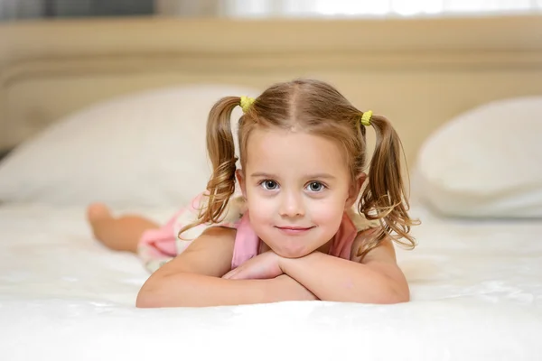 Little girl on the bed at home among the pillows — Stock Photo, Image