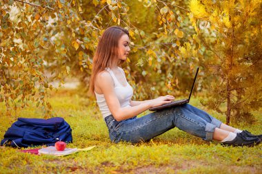 Öğrenci kız bir bilgisayarla çimenlerin üzerinde