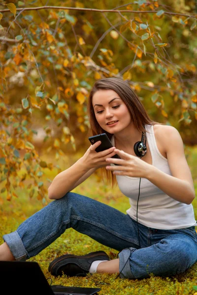 Młoda dziewczyna z długimi włosami w parku z telefonu komórkowego — Zdjęcie stockowe