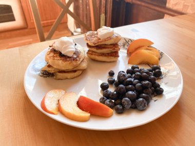 Beyaz tabakta yaban mersinli krep, yaban mersini ve şeftali dilimleri.