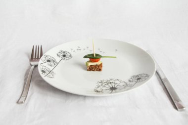 Beyaz bir arka planda, beyaz bir tabakta üzerinde avokado ve vişneli domates dilimleri olan yuvarlak bir somun var.