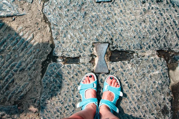 Female feet in tourist sandals stand on stone slabs