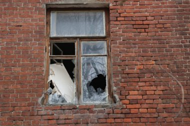 Terk edilmiş bir evin duvarında kırık camlar olan bir pencere.