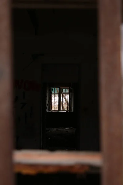 A window with broken glass in the wall of an abandoned house, through which you can see the window on the opposite side. Concept: there is a way out, light at the end of the tunnel, hope