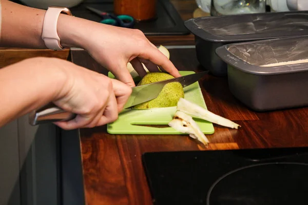 Kız yeşil bir kesme tahtasındaki armudu dilimler halinde kesiyor, eller kapalı.