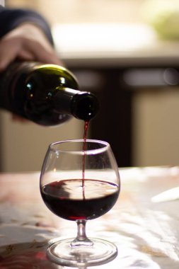 Bir adam kırmızı şarabı şişeden bardağa dolduruyor.