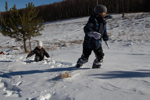 A boy runs through a snow field, falling into the snow, and laughs merrily