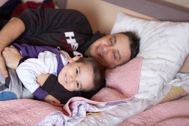 Baba ve oğul yataktalar, gülümsüyorlar ve sarılıyorlar. Gizli aile. 