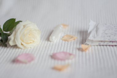 Beyaz arka planda bir kadın hijyenik tamponu, hijyenik pedler, gül ve gül yaprakları etrafa saçılmış. 