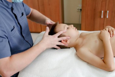 Çocuk doktorun muayenehanesinde kanepede yatıyor, doktor dış muayeneyi yapıyor. 